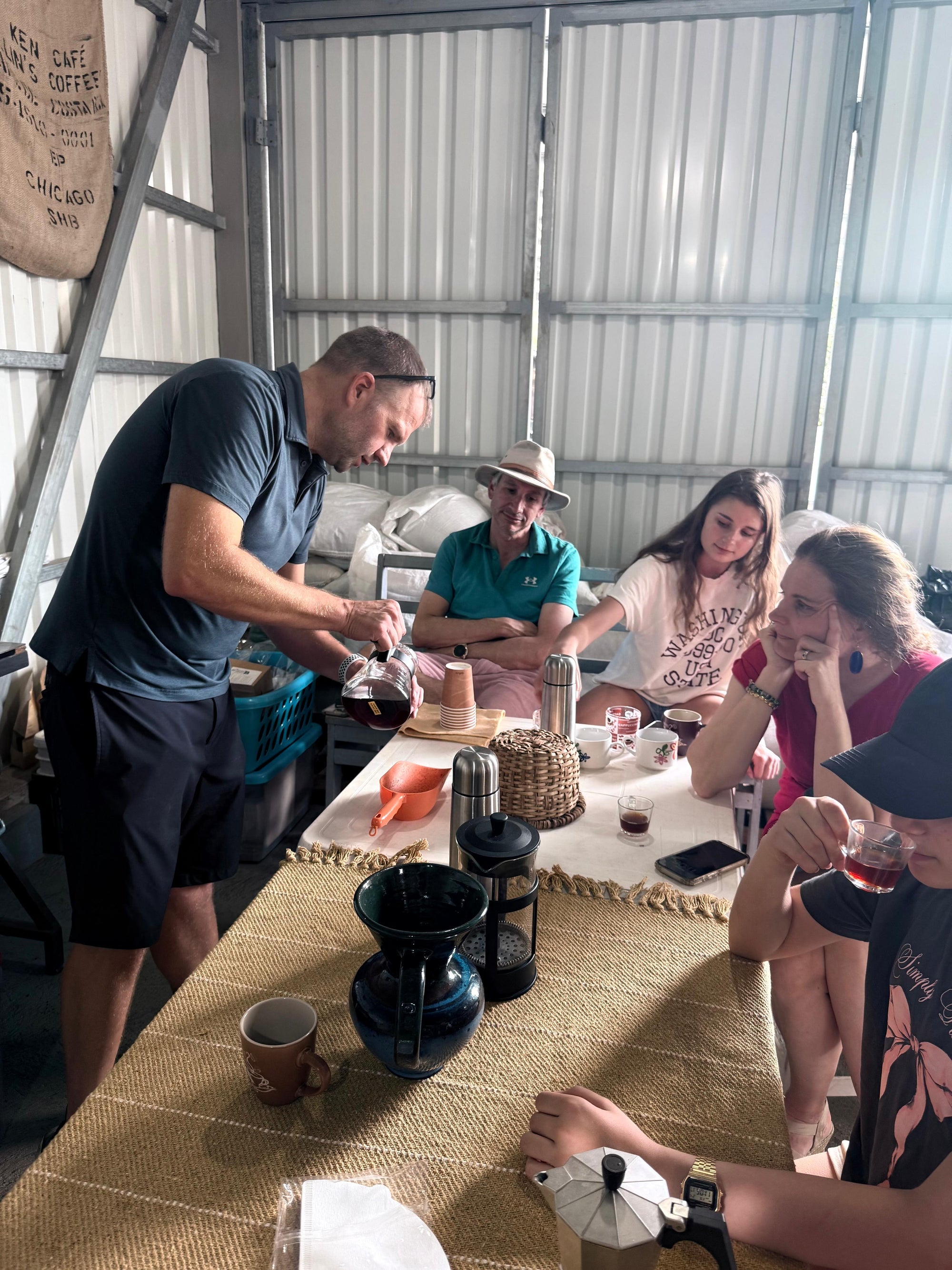 Group of people around a table in a rustic setting, possibly a coffee farm or workshop.